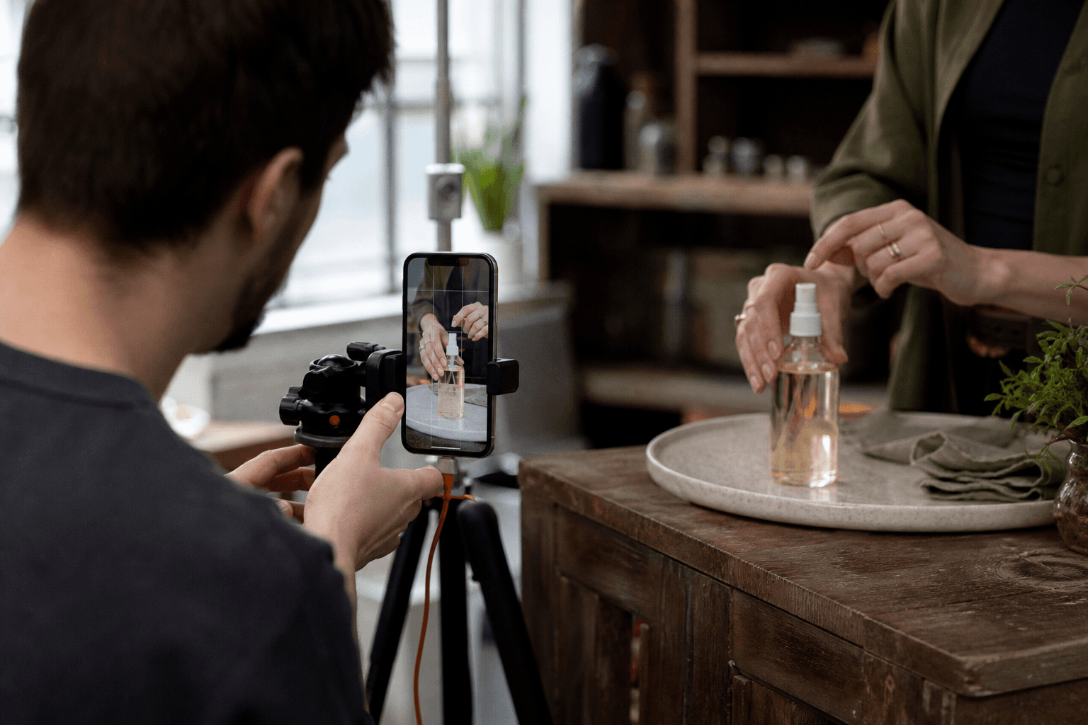 A creator demo shoot for a household product, showing hands, product close-up, phone monitor with vertical crop, and annotation about keeping the proof shot in frame; natural studio scene.